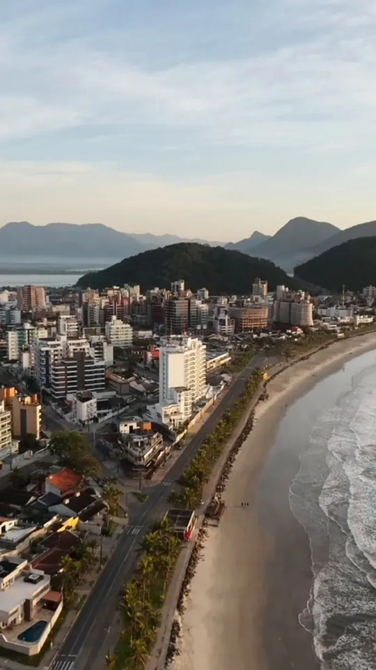 Vista aérea da orla, edifícios, praia e morros ao fundo